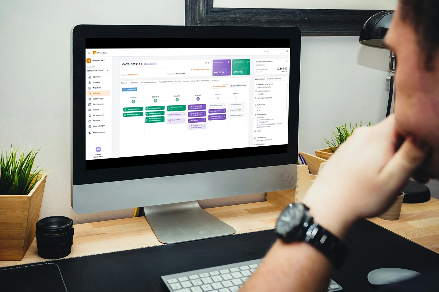 Mitarbeiter blickt auf einen Monitor mit der Warenwirtschaft-Software WorkX von RMT Soft, die eine Auftragsübersicht mit Prozessschritten, Kundendaten und Verkaufspreis für ein Küchenprojekt anzeigt.